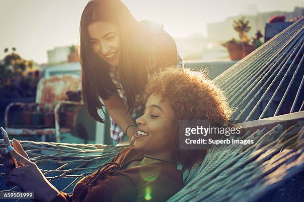 friends sharing smartphone on urban rooftop - hammock phone stock pictures, royalty-free photos & images