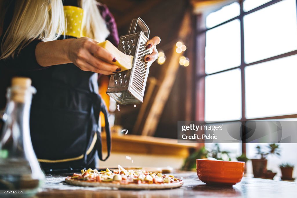Women hand grating the cheese on the pizza