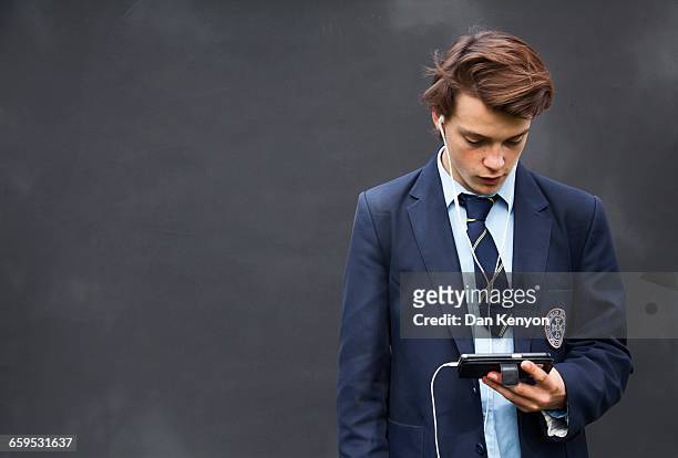 school boy with headphones and handheld device - school uniforms stock-fotos und bilder