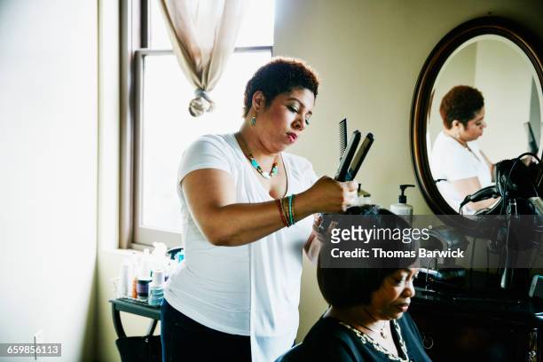 salon owner straightening hair of client in salon - hairdressers black woman stockfoto's en -beelden