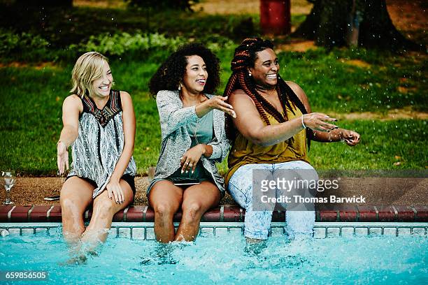 women sitting on edge of pool splashing friends - body positive stockfoto's en -beelden