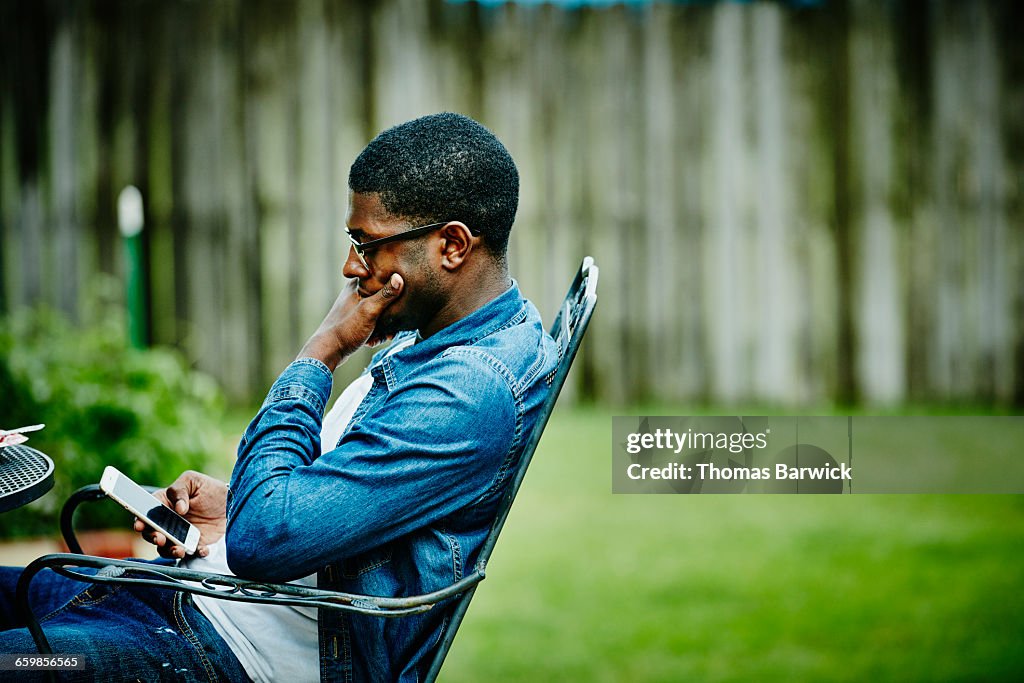 Man seated in backyard checking smartphone