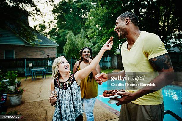 smiling woman offering friend dessert during party - holiday party candid stock pictures, royalty-free photos & images