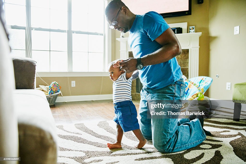 Father helping infant son learn to walk in home