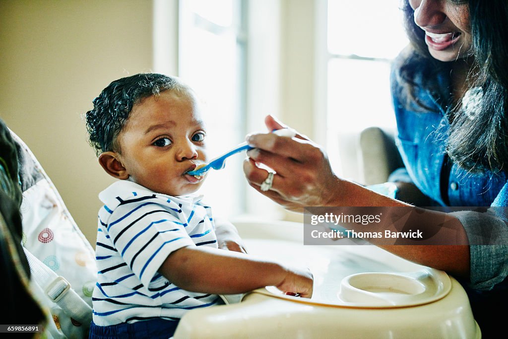Mother feeding infant son in highchair in home