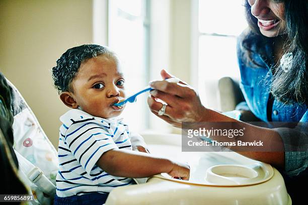 Mother feeding infant son in highchair in home