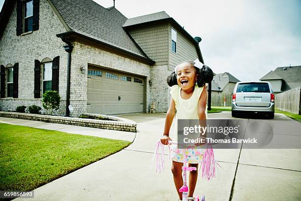 smiling young girl riding scooter in driveway - einfahrt stock-fotos und bilder