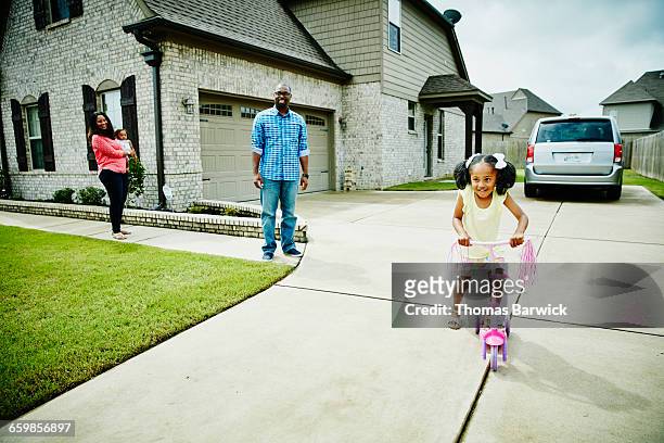 mother and father watching young daughter play - car in driveway stock-fotos und bilder