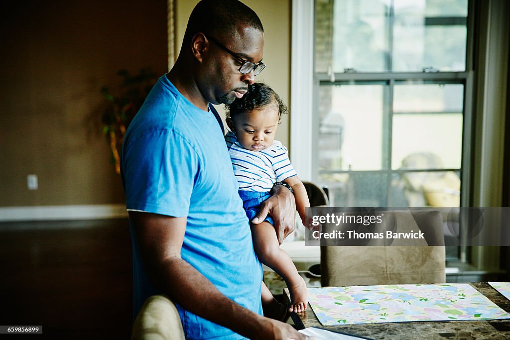 Father holding infant son while setting table