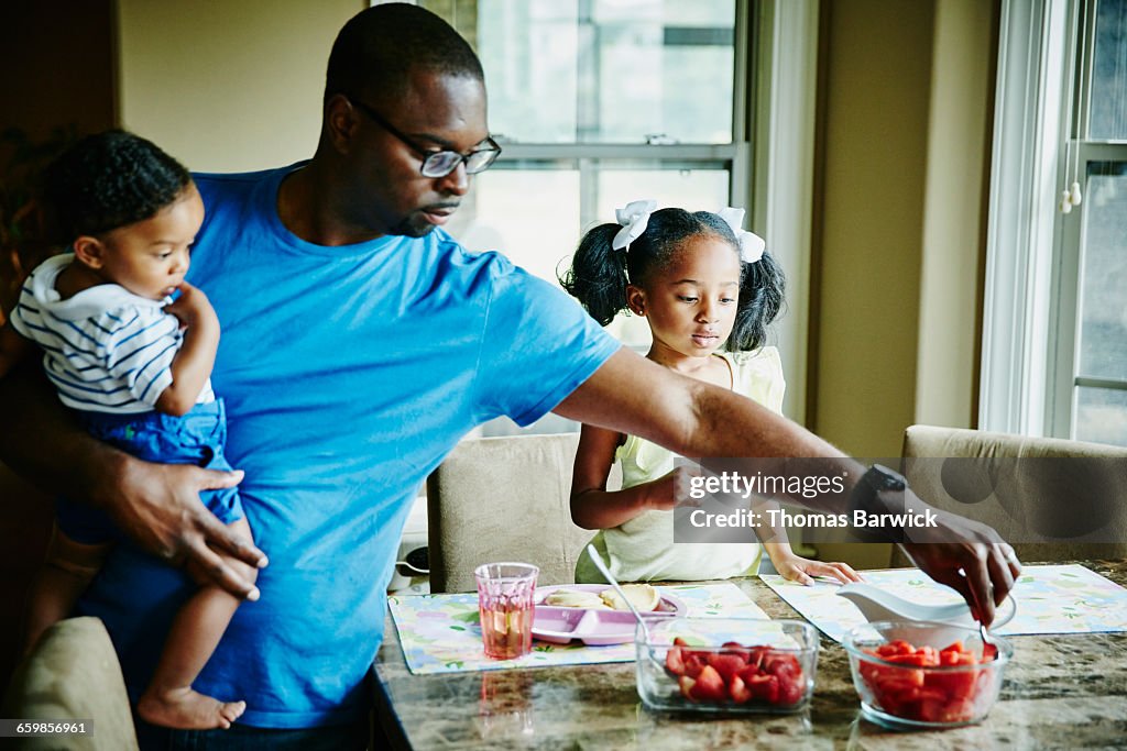 Father holding infant son while serving breakfast