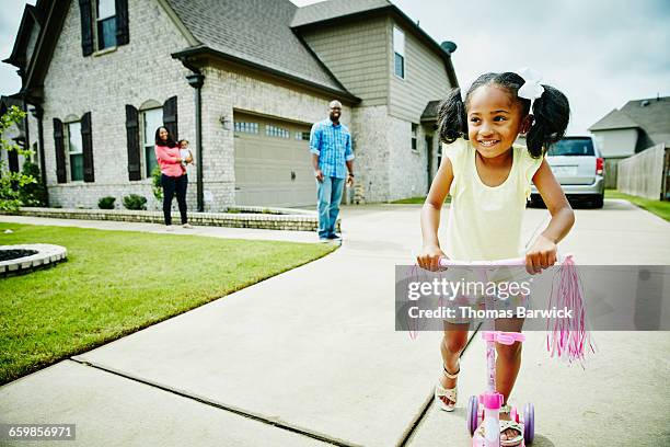 smiling young girl riding scooter in driveway - family of four in front of house stock-fotos und bilder