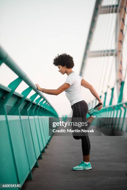 athletic, young woman exercising on city bridge - leg stretch girl stock-fotos und bilder