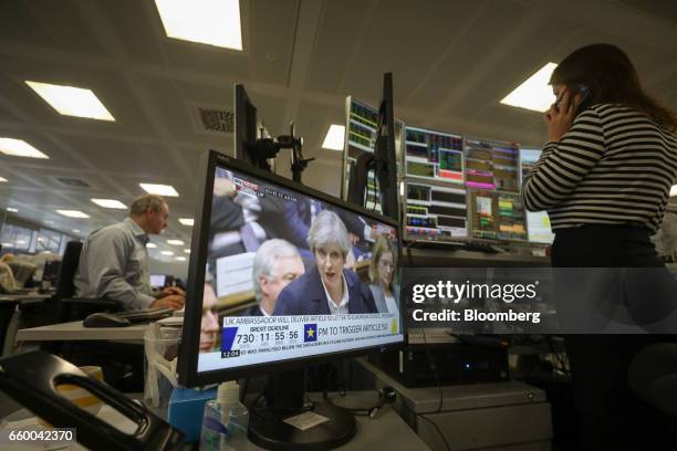 Television screen displays a news channel showing U.K. Prime Minister Theresa May speaking in the House of Commons, as a broker monitors financial...