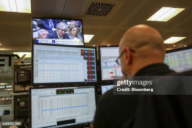 Television screen displays a news channel showing U.K. Prime Minister Theresa May speaking in the House of Commons, as a broker monitors financial...