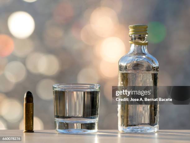 bottle of gin close to a bullet, concept of which the alcoholism kills - borracho foto e immagini stock