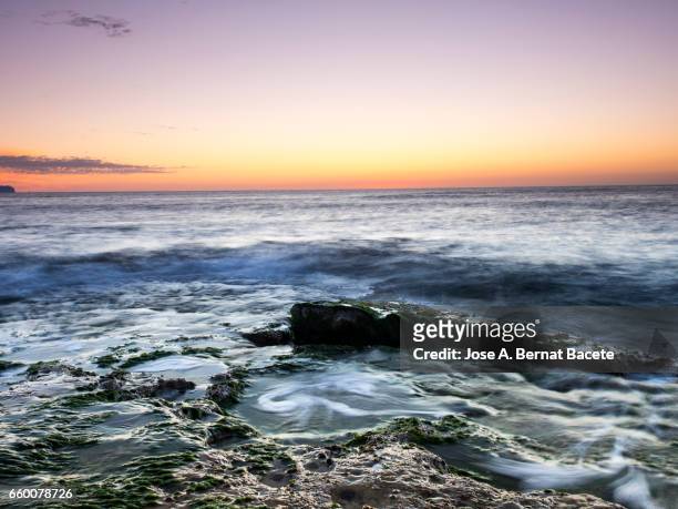exit of the sun of orange color, on the surface of the sea, in a zone of coast with rocks and waves in movement - paisaje espectacular - fotografias e filmes do acervo