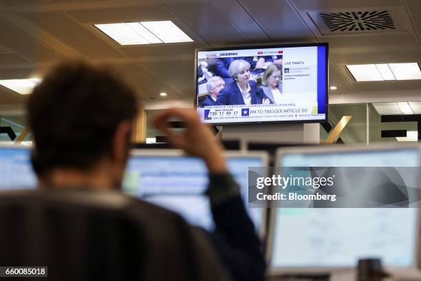 Television screen displays U.K. Prime Minister Theresa May speaking in the House of Commons, as a broker monitors financial data on computer screens...