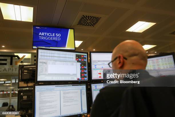 Television screen displays an alert saying article 50 has been triggered, as a broker monitors financial data on computer screens on the trading...