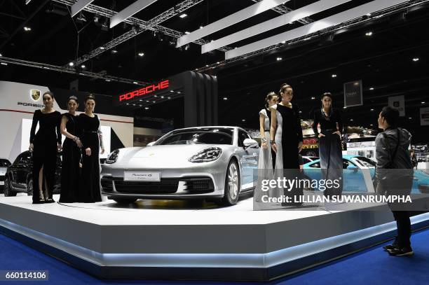 Models take directions from a photographer whilst surrounding a Porsche Panamera 4S car on display during the 39th Bangkok International Motorshow in...