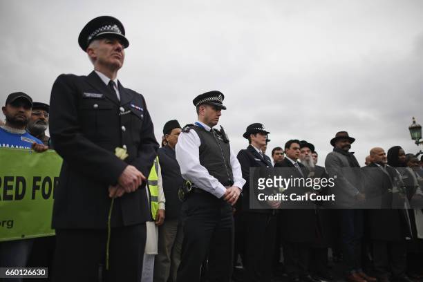Police officer and people hold roses on Westminster Bridge as they attend a vigil to remember the victims of last week's Westminster terrorist attack...