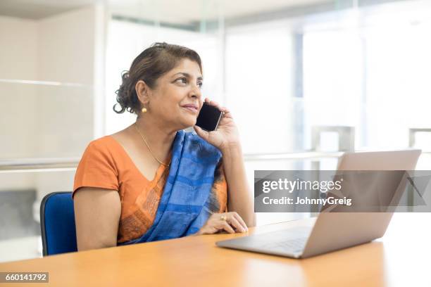 mature woman on the phone in office with laptop - sri lankan ethnicity stock pictures, royalty-free photos & images