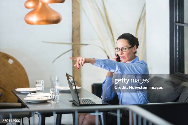 schöne brünette geschäftsfrau auf mittagspause, arbeiten am laptop im restaurant. sie trägt brille, im gespräch mit handy - brunette sitting at desk stock-fotos und bilder