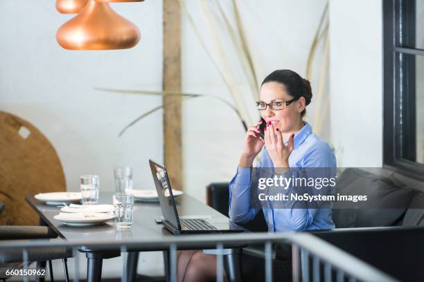 schöne brünette geschäftsfrau auf mittagspause, arbeiten am laptop im restaurant. sie trägt brille, im gespräch mit handy - brunette sitting at desk stock-fotos und bilder