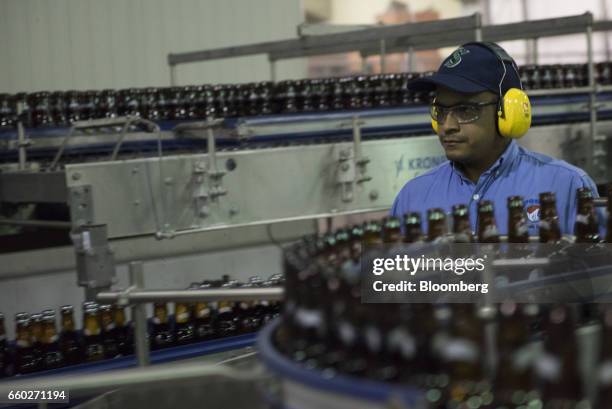 An employees watches as Empresas Polar SA beer bottles move along a conveyor belt after being filled during the production process at the Cerveceria...