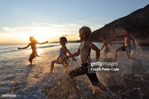 children running into sea at sunset - duchess of cornwall stockfoto's en -beelden