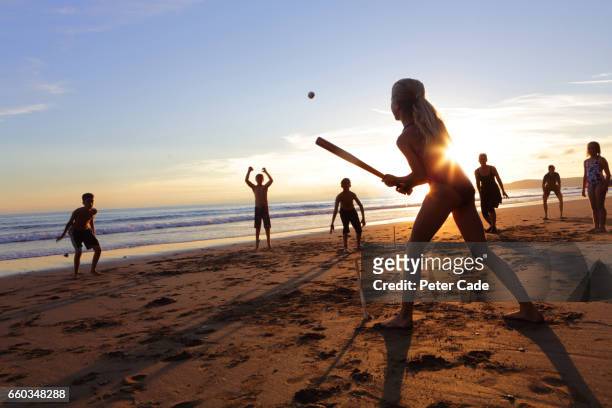group of children and adults playing ball game on beach at sunset - batting sports activity - fotografias e filmes do acervo