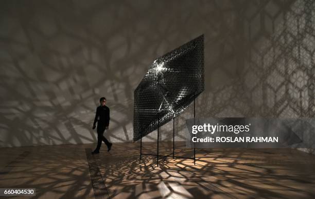 Museum staff member walks past an artwork by British artist Conrad Shawcross entitled "Slow Arc Inside a Cube VIII" exhibited during the Universe and...