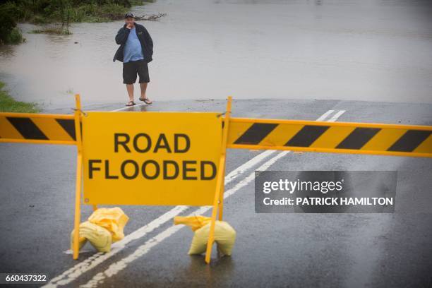 An onlooker looks at floodwaters washing over a closed road in Brisbane on March 30, 2017. Torrential rain hampered relief efforts after powerful...