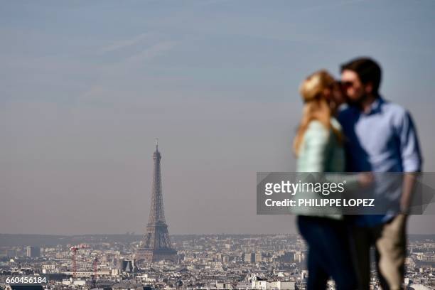 Woman kisses a man at a viewpoint overlooking the Effeil tower in Paris on March 30, 2017. / AFP PHOTO / Philippe LOPEZ