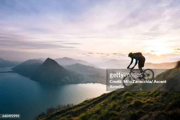 mountain biker descends steep mountain slope above lake - avventura foto e immagini stock