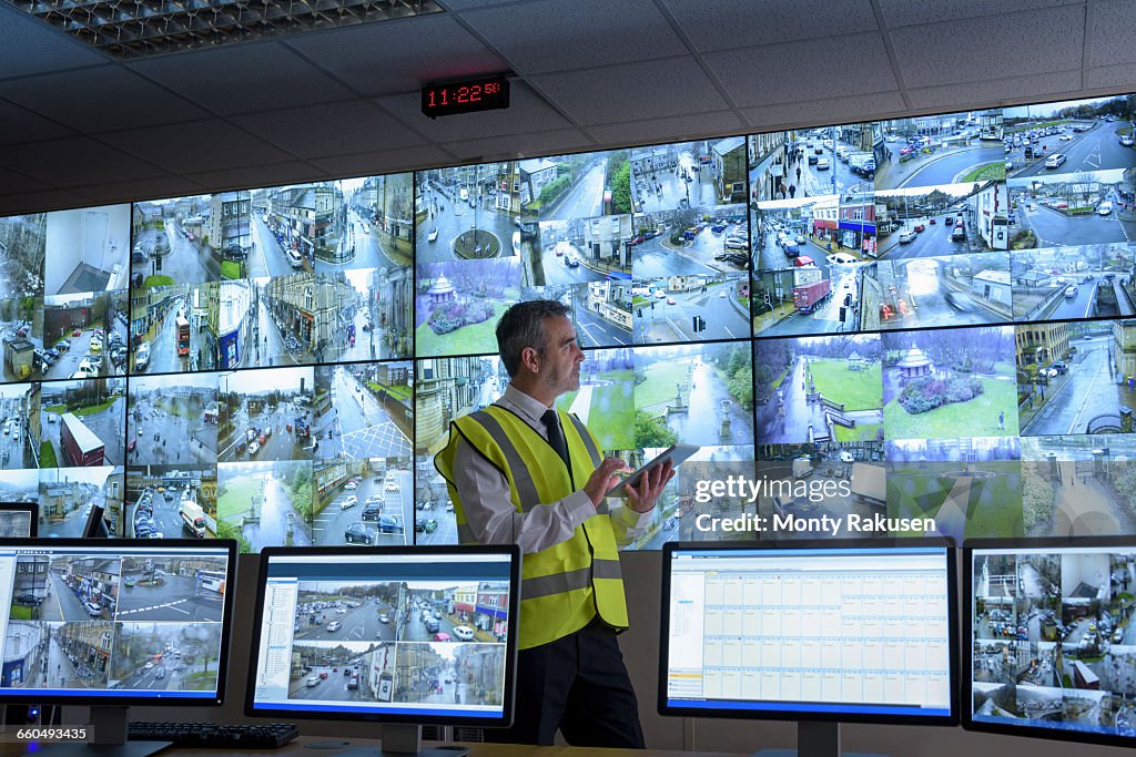 Security guard using digital tablet in security control room with video wall