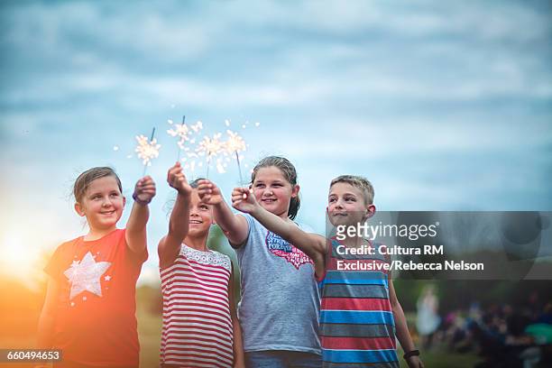 four friends holding lit sparklers in air at fourth of july celebration - cultura americana stock-fotos und bilder