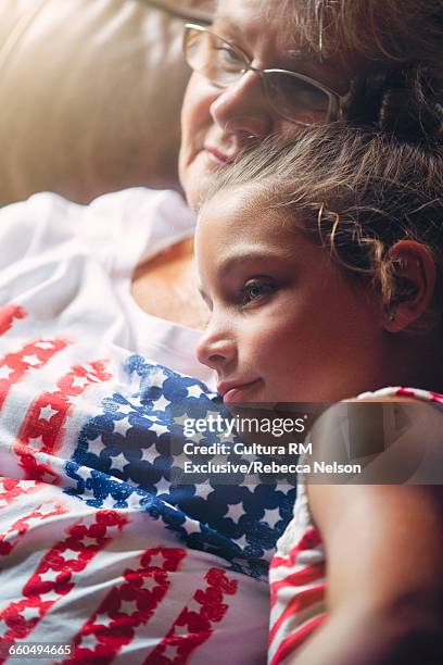 grandmother and granddaughter snuggling on couch at fourth of july party, wearing patriotic clothing - cultura americana stock-fotos und bilder