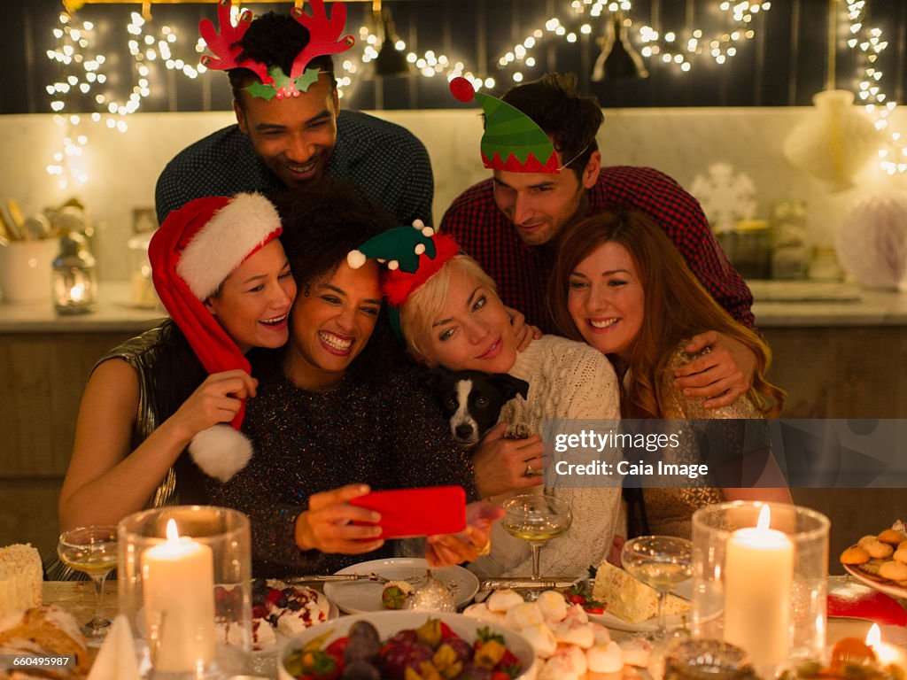 Playful friends with dog taking selfie at candlelight Christmas table