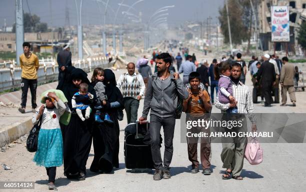 Iraqis fleeing their homes in Mosul's old city carry their belongings as they leave the fighting area on March 30 due to the ongoing battles between...