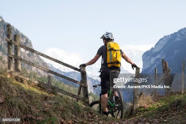 mountain biker pauses on mountain trail beside fence, looks off - short de cycliste photos et images de collection