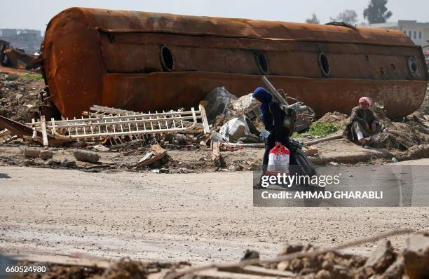 An Iraqi fleeing her home in Mosul's old city walks past a damaged vehicle as she leaves the fighting area on March 30 due to the ongoing battles...