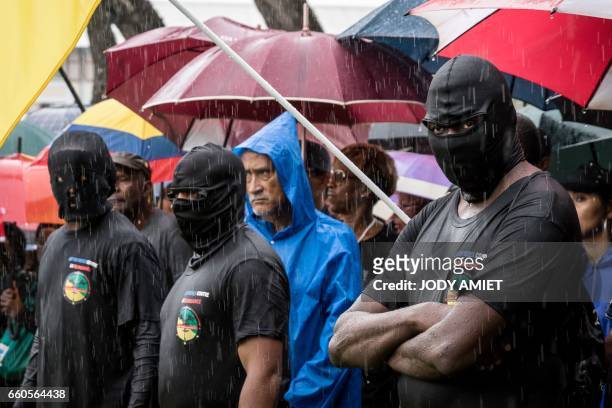 Members of the collective "500 freres" stand in front of a crowd gathered outside the prefecture in Cayenne on March 30 in support of the collective...
