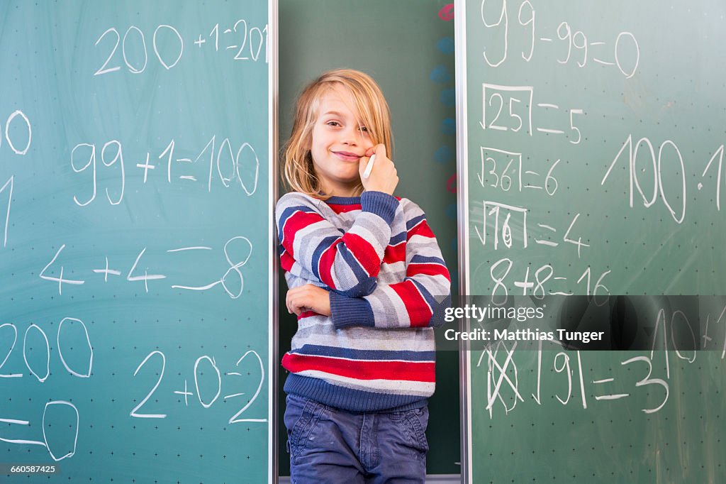 Young school boy standing in front of a blackboard