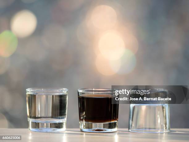 glasses of crystal of chupito one full and another emptiness  , illuminated by the light of the sun - alcoholismo photos et images de collection