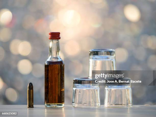 bottle of whiskey and  glasses of chupito close to a bullet , concept of which the alcoholism kills - eutanasia stock-fotos und bilder