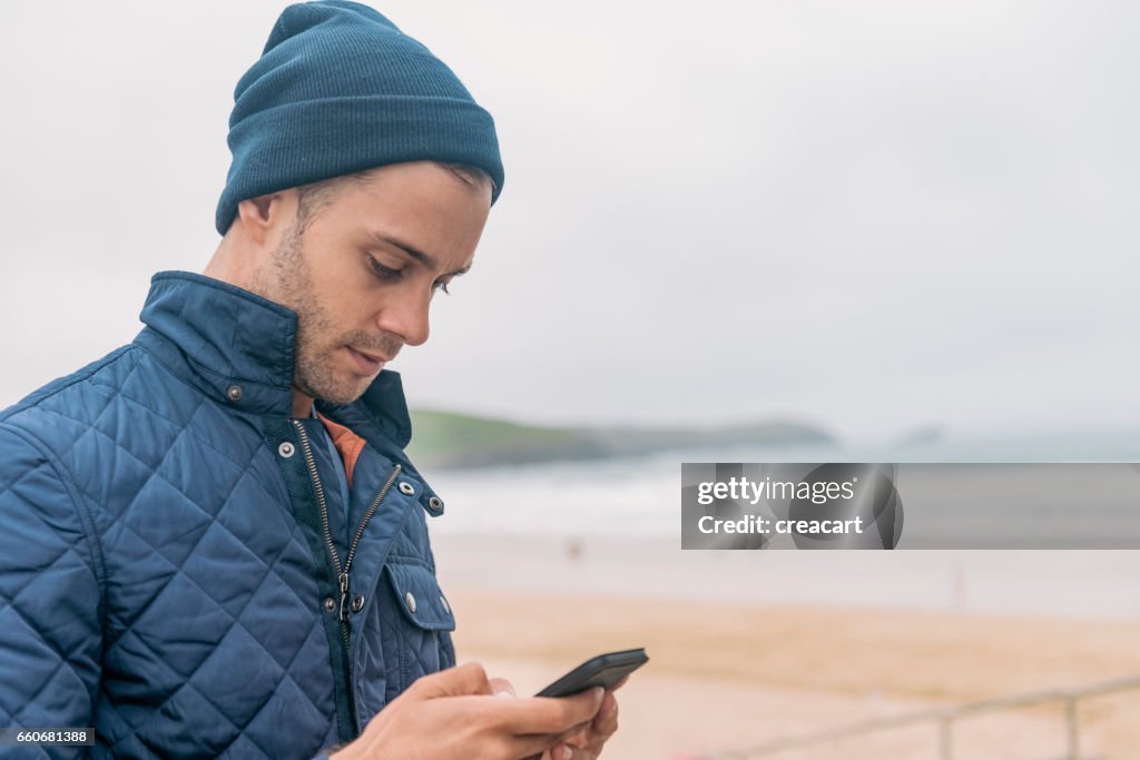 Envoyer des SMS sur son mobile à surplombant Fistral Beach, Newquay, Cornwall homme.