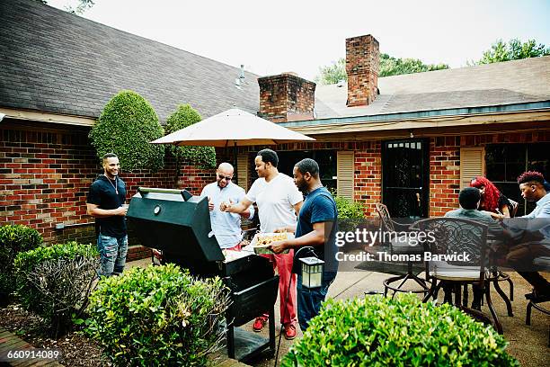 laughing friends barbecuing in backyard - fiesta de jardín fotografías e imágenes de stock