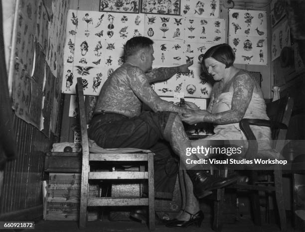 Heavily tattooed women applies a new tattoo to an equally tattooed man, 1920s or 1930s.