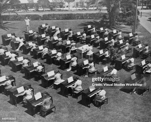 Conductor Richard Dickson directs is shown directing the forty, female spinet musicians as the rehearse outdoors for a Music Week performance, Long...