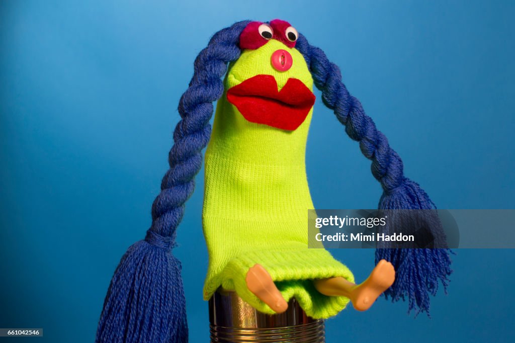 Green Sock Puppet with Blue Braids Sitting on Tin Can